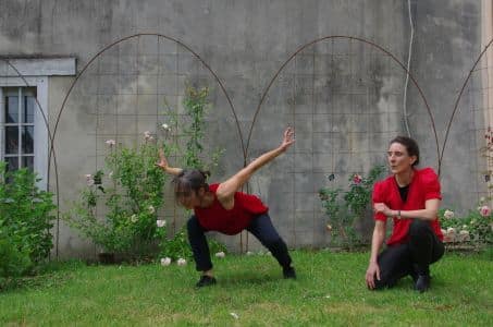 Photo de "Tomber comme le jour", spectacle de Cécile Geay : deux femmes en rouge et noir dansent dans un jardin
